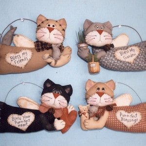 May include: Four handmade cat angel ornaments with wings and a heart-shaped message on each. The cats are holding a mouse, a potted plant, a heart, and a kitten. The messages read "Bless My Friends", "Bless My Garden", "Bless Your Purr-fect Heart", and "Purr-fect Blessings".