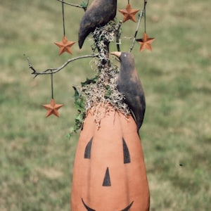 Puede incluir: Una decoración de Halloween hecha a mano con una calabaza con una cara sonriente, dos cuervos negros posados en una rama con estrellas marrones colgando de las ramas.