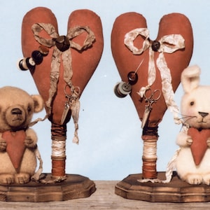 May include: Two handmade fabric hearts on wooden stands, each with a teddy bear and a bunny holding a smaller heart. The hearts are decorated with buttons, ribbon, and scissors.