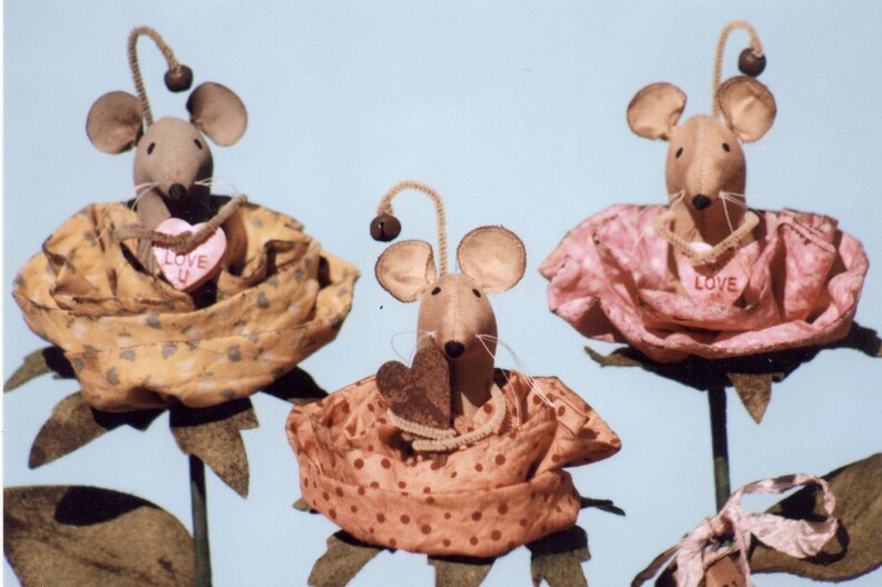 May include: Three handmade fabric mouse figurines, each holding a heart-shaped decoration. The mice are dressed in fabric roses, one yellow, one pink, and one orange. The hearts have the words "Love You" and "Love" printed on them.