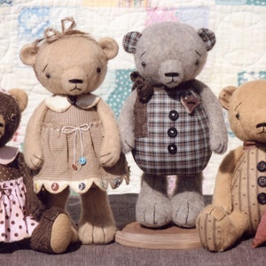 May include: Four handmade teddy bears wearing different patterned dresses and shirts. The bears are sitting on a quilt with a variety of colors and patterns.