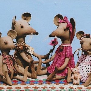 Pode incluir: Quatro bonecas de rato de tecido feitas à mão sentadas em um edredom de retalhos. Os ratos usam vestidos e uma camisa xadrez. Um rato está segurando um pequeno animal de pelúcia.