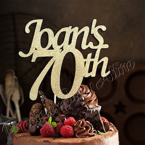 May include: Gold glitter cake topper with the text "Joan's 70th" on a chocolate cake with raspberries and chocolate decorations.