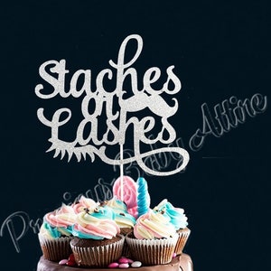 May include: A silver glitter cake topper with the text "Staches or Lashes" and a glitter mustache. The topper is on top of a chocolate cake with pink, white, and blue frosting and cupcakes.