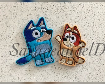 May include: Two embroidered patches featuring cartoon dog characters. One is blue with black accents, the other is tan with red accents. Both have detailed stitching and are likely for clothing or accessories.