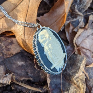 以下が含まれることがあります： 銀色のチェーンネックレスに、黒と白のカメオペンダントがついた、フクロウのデザイン。ペンダントは銀色のワイヤーフレームで囲まれています。