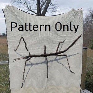May include: A white crochet blanket with a brown stick insect design. The blanket has the text "Pattern Only" printed on it.
