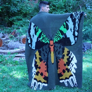 May include: A green crocheted blanket with a large butterfly design in shades of green, white, black, orange, and yellow.