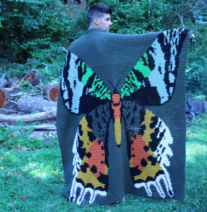 May include: A green crocheted blanket with a large butterfly design in shades of green, white, black, orange, and yellow.