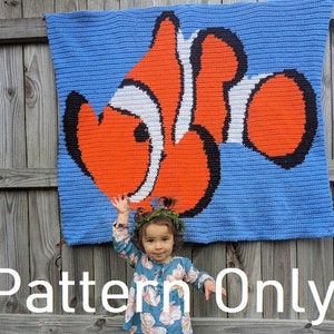 May include: A crochet pattern for a colorful clownfish blanket. The pattern is shown on a blue background with a white border. The pattern is for sale, but the blanket is not included.