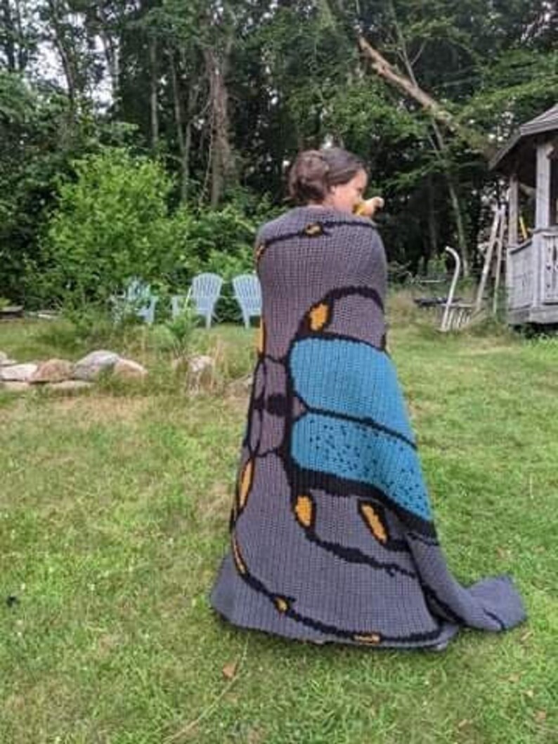 May include: A person wearing a gray crocheted blanket with a blue and yellow butterfly design.