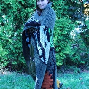 May include: A person is wrapped in a large, colorful crochet blanket with a variety of colors and patterns. The blanket features a large, orange and yellow design in the lower right corner.