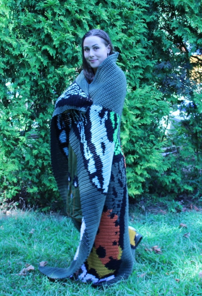 May include: A person is wrapped in a large, colorful crochet blanket with a variety of colors and patterns. The blanket features a large, orange and yellow design in the lower right corner.