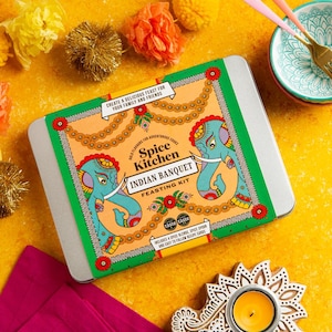 May include: A rectangular silver metal tin featuring a label with the text Spice Kitchen Indian Banquet Feasting Kit. The label displays two teal elephants, orange floral garlands, and green borders on a light orange background.