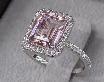Könnte beinhalten: Ein silberner Ring mit einem großen, rechteckigen, hellrosa Edelstein, der von einem Heiligenschein aus kleineren Diamanten umgeben ist. Die Ringschiene ist ebenfalls mit kleineren Diamanten besetzt.
