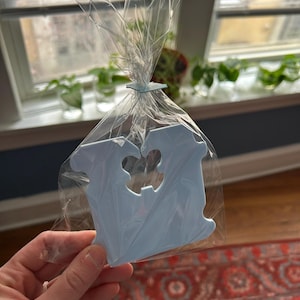 May include: A light blue plastic letter V with a heart cut out of the center. The letter is packaged in a clear plastic bag and tied with a twist tie.