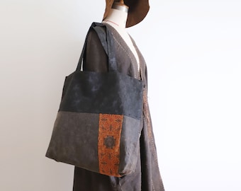 May include: A black and gray tote bag with a brown and orange patterned fabric panel. The bag has a wide, flat base and two top handles.