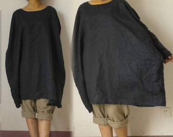 Puede incluir: Una túnica de lino negra de gran tamaño con un corte holgado y un escote redondo. La modelo lleva la túnica con pantalones cortos color caqui remangados.