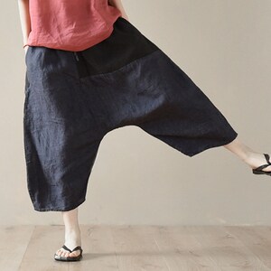 May include: A pair of loose-fitting, dark blue linen pants with a black patch pocket on the front. The pants have a wide leg and a cropped length.