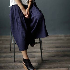 May include: A woman wearing a dark blue linen skirt with a loose, flowing fit. The skirt is knee-length and has a simple, elegant design.