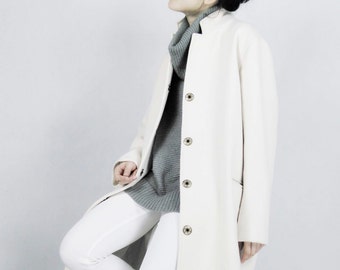 May include: A long, off-white coat with large buttons, paired with white pants and a gray turtleneck. The outfit is completed with gray ankle boots. The coat has a simple, elegant design, suitable for a variety of occasions.