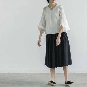 May include: A white linen top with a scoop neck and 3/4 sleeves paired with a black midi skirt.