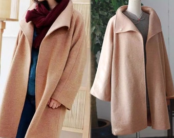 May include: A light brown, oversized coat with a wide collar. The coat is displayed on a person and a mannequin. The coat has a simple, elegant design, with a long length and a relaxed fit. The fabric appears to be a soft wool blend.