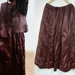 Puede incluir: Una falda plisada color burdeos con una cintura ancha. La falda está hecha de una tela brillante, similar al satén.