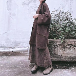 May include: A brown long-sleeved cardigan with a high collar and a skirt. The cardigan has a ribbed texture and a slightly loose fit. The skirt is a midi length and has a similar ribbed texture. The person is wearing brown boots.