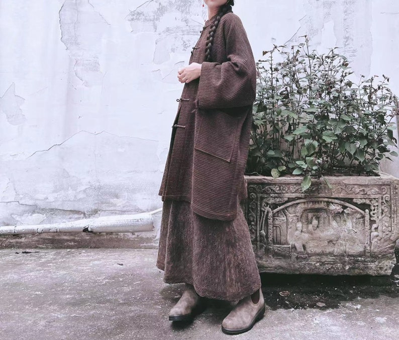May include: A brown long-sleeved cardigan with a high collar and a skirt. The cardigan has a ribbed texture and a slightly loose fit. The skirt is a midi length and has a similar ribbed texture. The person is wearing brown boots.