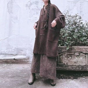 May include: A brown, long-sleeved, button-up cardigan with a mandarin collar and a single button closure. The cardigan has a relaxed fit and is made of a soft, textured fabric.