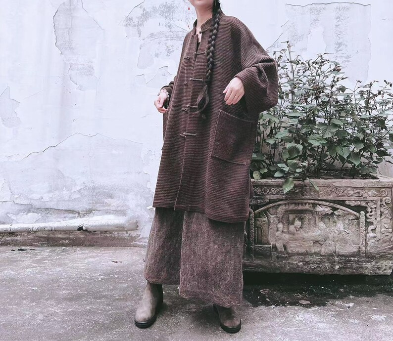 May include: A brown, long-sleeved, button-up cardigan with a mandarin collar and a single button closure. The cardigan has a relaxed fit and is made of a soft, textured fabric.