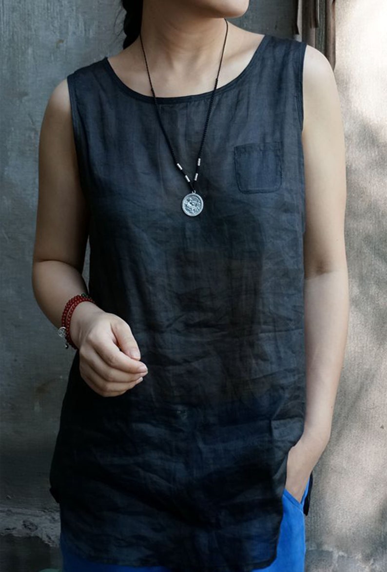 May include: A sleeveless black linen top with a small pocket on the left side. The model is wearing a silver necklace with a round pendant.