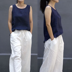 May include: Two women wearing a navy blue sleeveless top with white wide-leg pants. The pants have a drawstring waist.