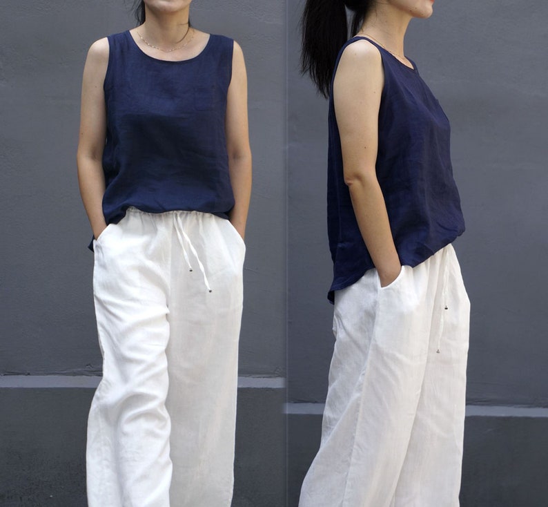 May include: Two women wearing a navy blue sleeveless top with white wide-leg pants. The pants have a drawstring waist.