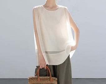 May include: A sleeveless, cream-colored top with a sheer overlay. The top has a round neckline and a slightly longer back hem. The person is holding a woven tote bag with brown leather handles. The person is wearing olive green pants.