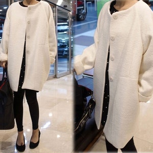 May include: A white long-sleeved coat with a button closure and a slightly oversized fit. The coat has a simple design and is made of a soft, textured fabric.