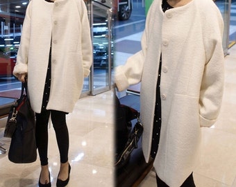 May include: A white long-sleeved coat with a button closure and a slightly oversized fit. The coat has a simple design and is made of a soft, textured fabric.