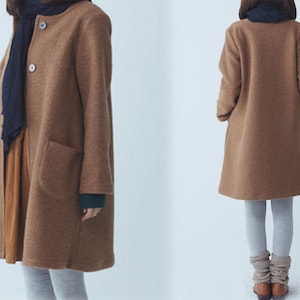 May include: A long-sleeved brown coat with a collar and pockets. The coat is worn over a grey shirt and grey trousers.