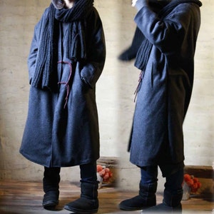 May include: A long, dark gray coat with a matching scarf. The coat has a simple design with a tie closure and pockets. The scarf is thick and knitted. The outfit is completed with black boots.