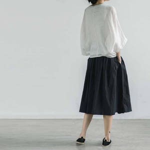 May include: A woman wearing a white, long-sleeved blouse with a black, knee-length skirt.