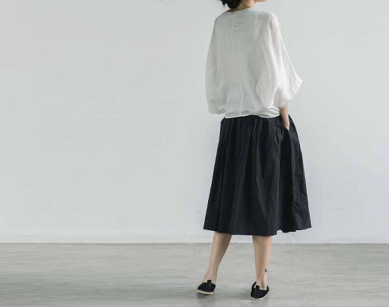 May include: A woman wearing a white, long-sleeved blouse with a black, knee-length skirt.