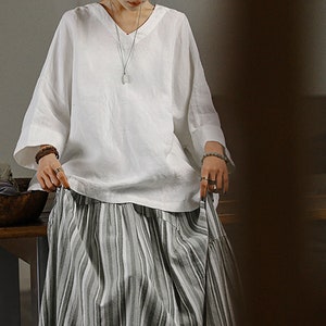 May include: A white linen blouse with a v-neck and 3/4 sleeves paired with a striped skirt. The skirt has a tiered design and is made of a lightweight fabric.