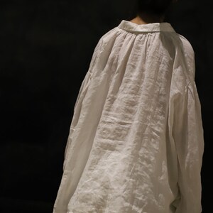 Pu&ograve; includere: Una camicia di lino bianca con una vestibilit&agrave; ampia e oversize e un collo arricciato. La camicia &egrave; indossata sopra pantaloni bianchi.