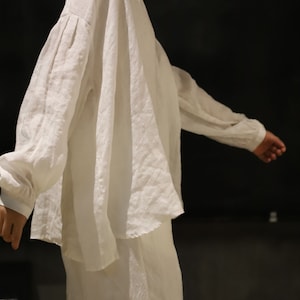 Pu&ograve; includere: Una camicia bianca di lino a maniche lunghe e vestibilit&agrave; rilassata. La camicia ha un aspetto leggermente drappeggiato sulle spalle e una lunghezza leggermente pi&ugrave; lunga sul retro.