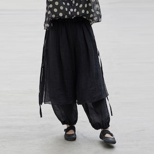 May include: Black wide-leg pants with a layered design and ankle-length hem. The pants have a loose, flowing fit and are paired with black shoes. The top is a sheer, polka-dot blouse.