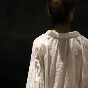 Pu&ograve; includere: Una blusa bianca ampia con scollo arricciato e maniche lunghe. La blusa &egrave; realizzata in un tessuto leggero e ha una vestibilit&agrave; rilassata.