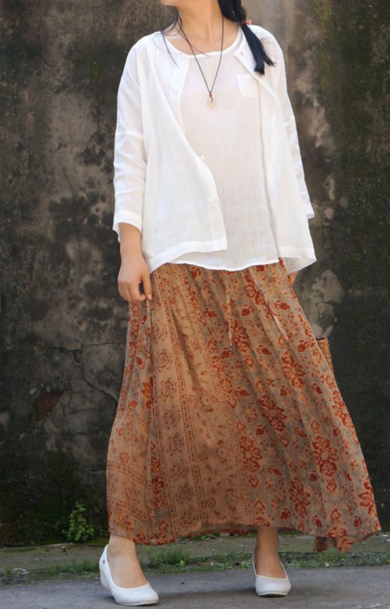 May include: A white linen shirt with a long sleeve and a brown and orange floral print skirt. The skirt has a long length and a flowy style.