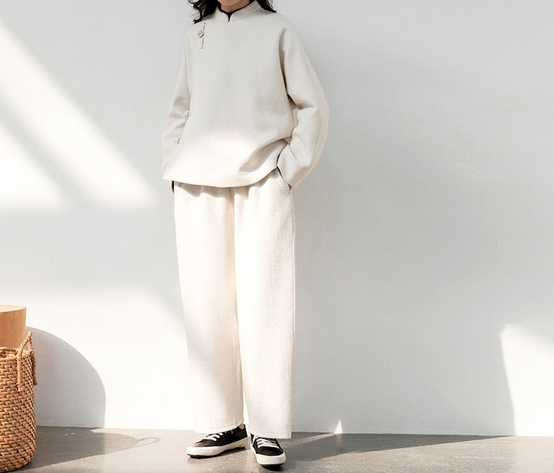 May include: A white long-sleeved top with a mandarin collar and a white pair of pants. The top has a button closure at the neck.