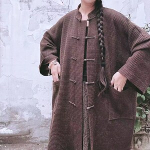 May include: A long brown waffle-textured coat with a mandarin collar and multiple buttons down the front. The coat has two large pockets on the sides.